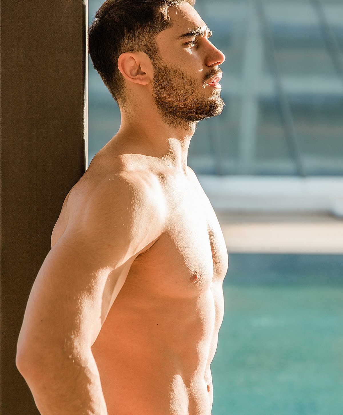 Man standing shirtless against a wall.