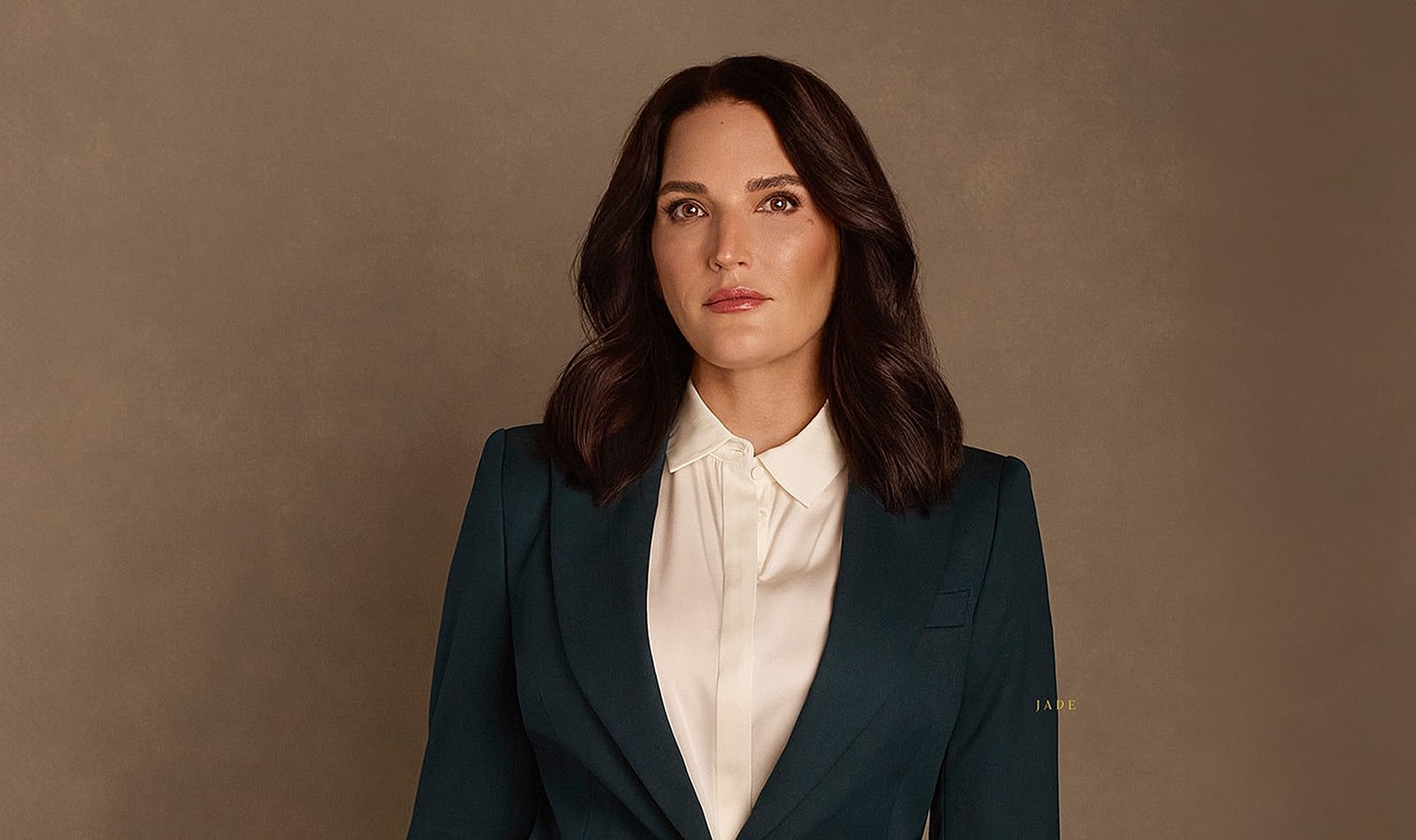Professional woman in formal attire against neutral background.