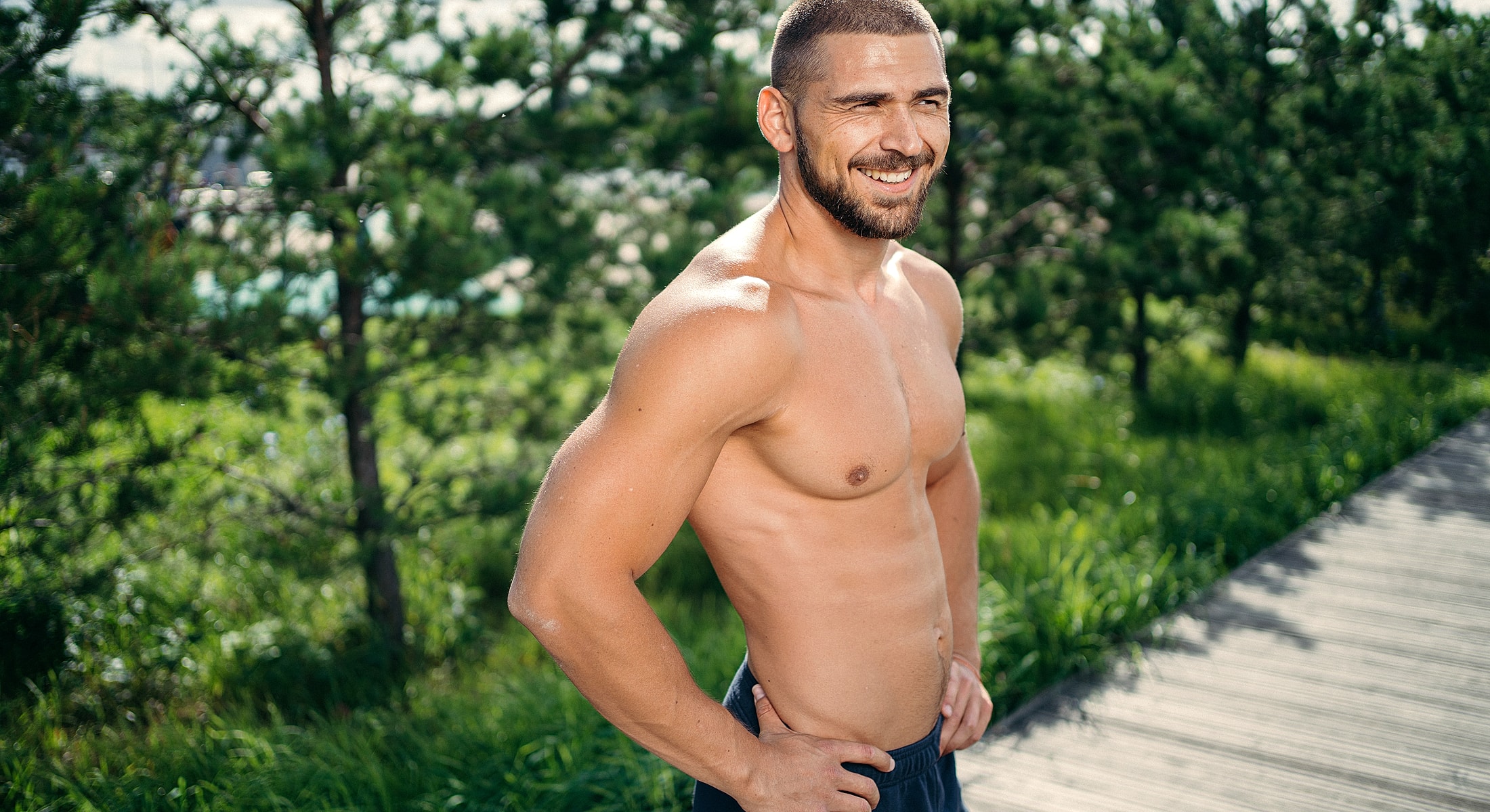 Smiling man standing outdoors, showcasing a fit physique.