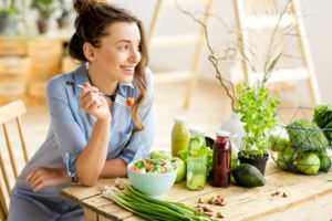 woman eating healthy salad sitting on the table with green fresh ingredients 